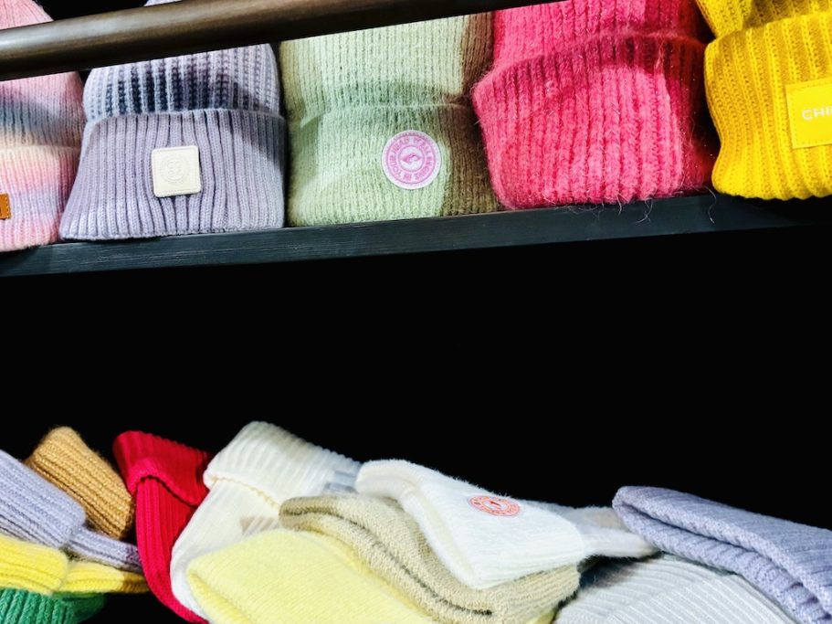 „Winteraccessoires – BSix® Conceptstore“ „Gestapelte Strickaccessoires und winterliche Mützen in Pastellfarben.“