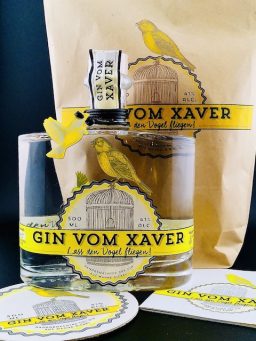 Gin vom Xaver – Geschenkset & Arrangement Abgebildetes Set aus „Gin vom Xaver“-Flaschen, gelben Akzenten, Untersetzern und dekorativem Hintergrund im Markenstil.