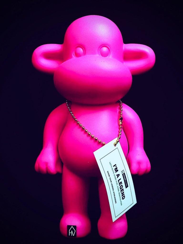I’M A LEGEND Pinkfarbene Kunststofffigur in humanoider Form mit Anhängeetikett vor dunklem Hintergrund