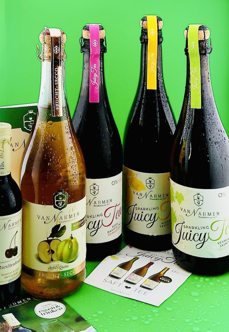 Alkoholfreie Fruchtsekt-Getränke in Glasflaschen Mehrere Flaschen alkoholfreier Fruchtsekt-Getränke verschiedener Sorten in Glasflaschen vor grünem Hintergrund